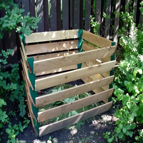 backyard compost bin garden: wooden slat composter surrounded by lush greenery and a wooden fence