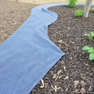 blue landscape fabric installation on mulch in a garden with young plants and tree trunk