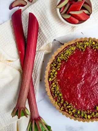 cherry red rhubarb stalks with green leafy ends and a tart featuring vibrant red rhubarb filling topped with pistachios
