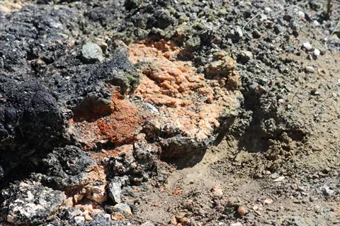 close-up of mineral-rich volcanic rock garden soil with porous dark rocks and orange mineral deposits, typical for desert/succulent habitats