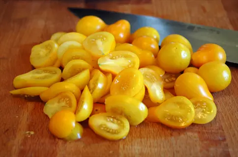cluster of whole and sliced yellow pear tomatoes on a wooden cutting board with chef's knife in background