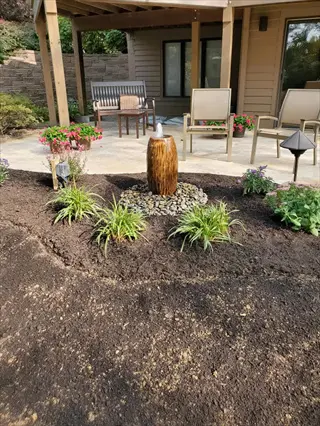 dark reflective mulch garden with water fountain, daylilies, and covered patio with outdoor furniture in a backyard setting