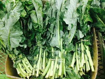 fresh bundles of leafy green vegetables (likely collard greens) with vibrant green leaves and thick stems, tied together in a cardboard container