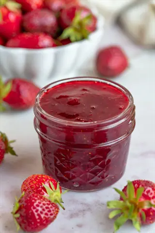jar of sparkle strawberry jam surrounded by fresh strawberries with a bowl of berries in background