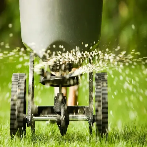 lawn fertilizer spreader dispersing grass treatment pellets on lush green yard