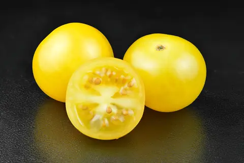 patio tomato yellow fruits (similar to patio choice yellow) on dark surface: two whole and one halved to show seeds and flesh