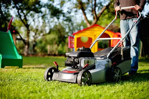 person using a lawn mower cutting grass in a backyard with playground equipment and trees
