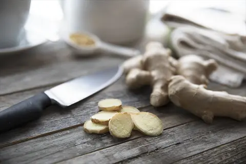 sliced ginger rhizomes next to a knife on a wooden surface