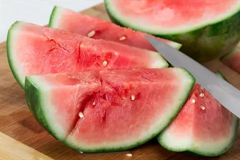 sliced seedless watermelon with red flesh on a wooden cutting board with a knife
