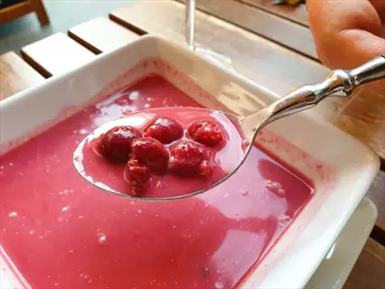spoon holding bright red meteor sour cherries over a bowl of pink cherry soup or dessert
