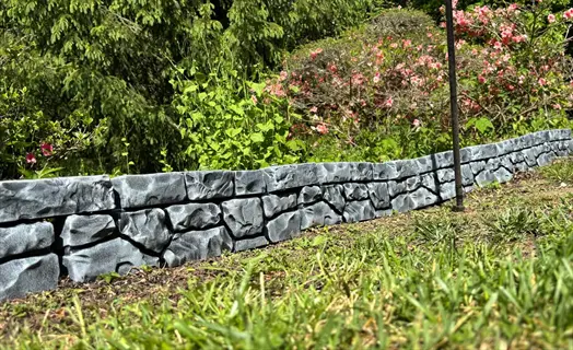 stone garden bed edging along grass with flowering bushes in the background