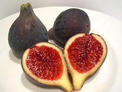 violette de bordeaux fig: whole dark purple figs and a halved fig with vibrant red flesh and seeds on a white plate
