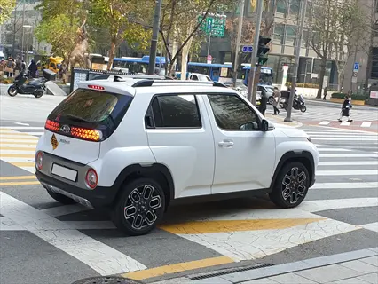white hyundai casper suv driving on an urban crosswalk with traffic lights and city buildings in the background