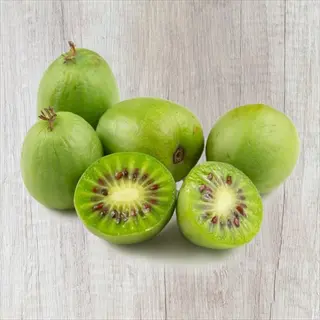 whole and halved issai kiwi berry (actinidia arguta) fruits showing vibrant green flesh with radiating black seeds on light wooden surface